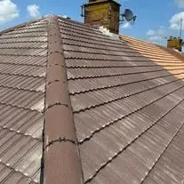 Finished pitched roof in brown tiles with a straight ridge and a chimney behind