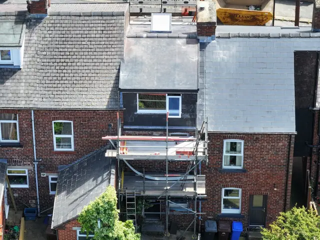 Drone view of the back of a brick terrace, with scaffolding around a newly built dormer clad in black between slate roofs