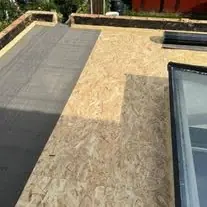 Flat roof half covered, with new covering laid over fresh boards beside a rooflight