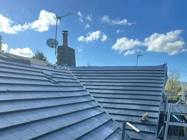New grey roof tiles running up to a chimney stack under a blue sky, with scaffolding along the edge of the roof