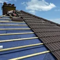 New dark grey tiles being laid up a pitched roof over battens, with a chimney at the top