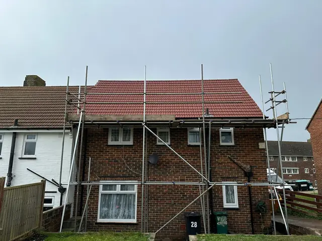Red tiled roof on a semi-detached house, with scaffolding along the eaves and up the side