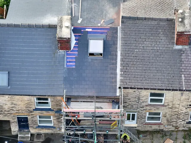 Drone view of a terrace roof being re-covered in slate, with blue membrane and battens where the new slates are still to go on, and scaffolding below